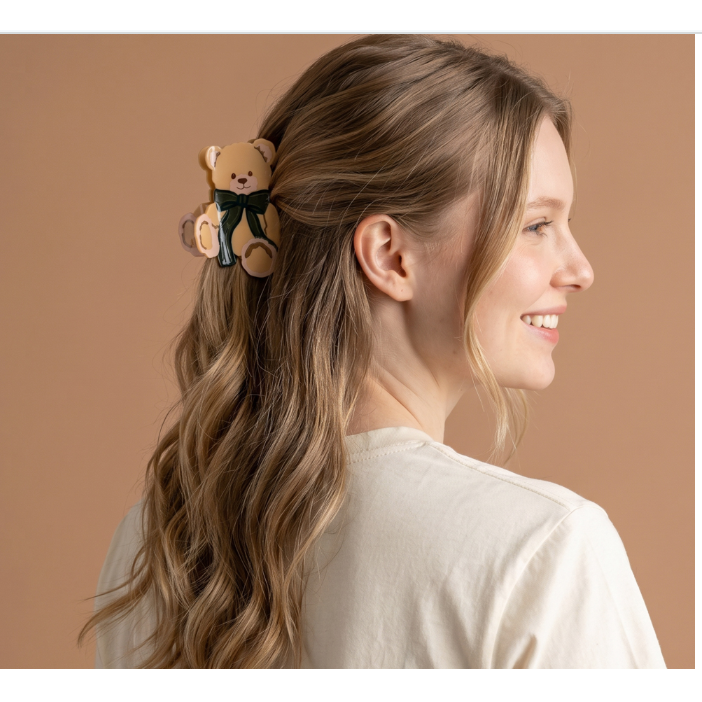 A woman with long wavy light brown hair wearing a small teddy bear hair clip. The hair clip is tan with a black bow.