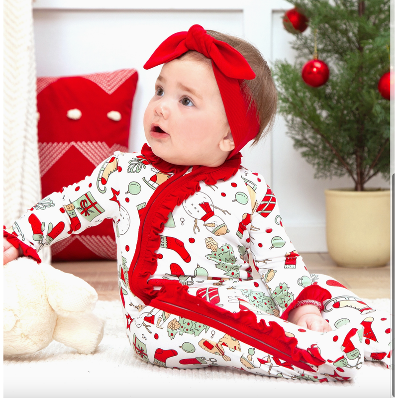 Baby in a festive outfit with red and white pattern, sitting on a soft surface.