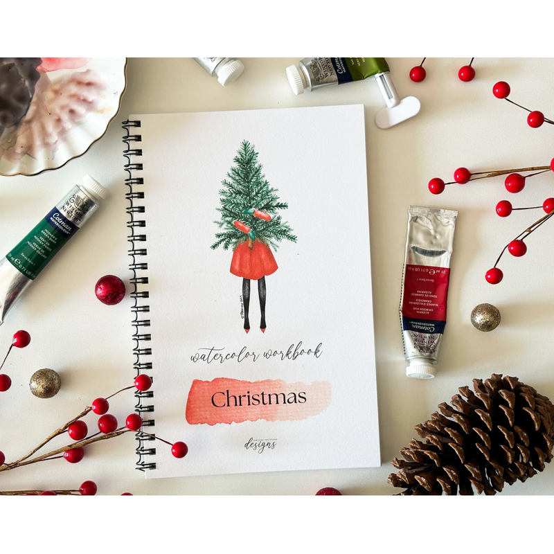 Watercolor workbook with Christmas design on a table with art supplies and decorations
