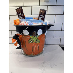Pumpkin-themed candy dish with Halloween treats on a white countertop.
