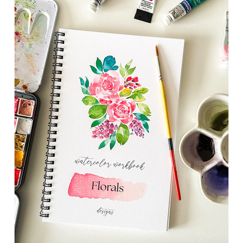 Watercolor workbook with floral design on a table with art supplies