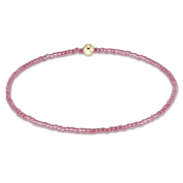 A delicate pink beaded bracelet with a small gold bead, displayed on a clean white background.