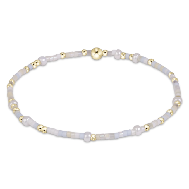 A delicate beaded bracelet with iridescent white and pale blue beads, accented by small gold spacer beads and a larger polished gold clasp, shown on a plain white background.