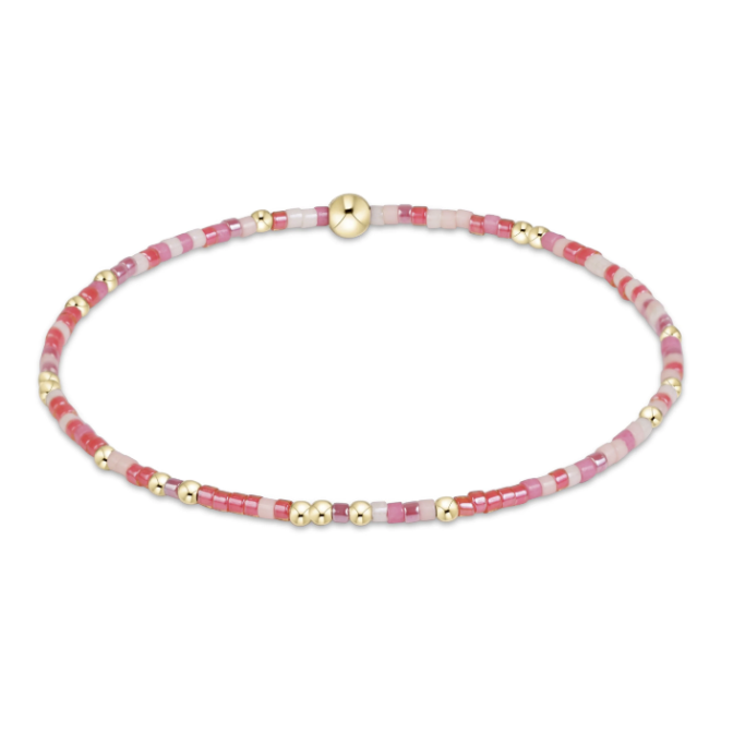 A beaded stretch bracelet featuring alternating pink and white beads with small gold spacer beads and a larger gold bead, shown on a plain white background.