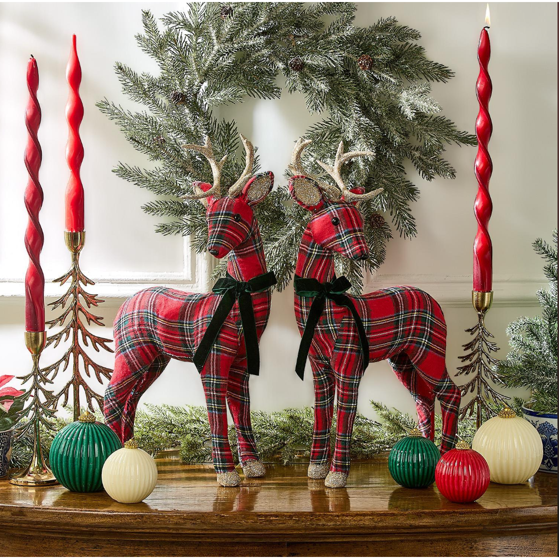 Two plaid deer figurines on a mantel with Christmas decorations including candles and wreaths.